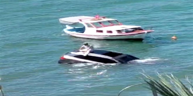 Denize uçan otomobilinin üzerinde oturup yardım bekledi